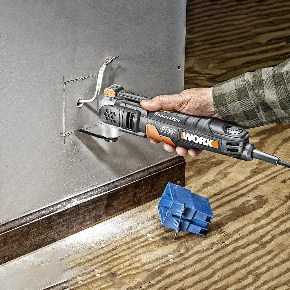 Bir el, metal yüzeyi kesen gri ve turuncu bir Worx Sonicrafter alet tutuyor.