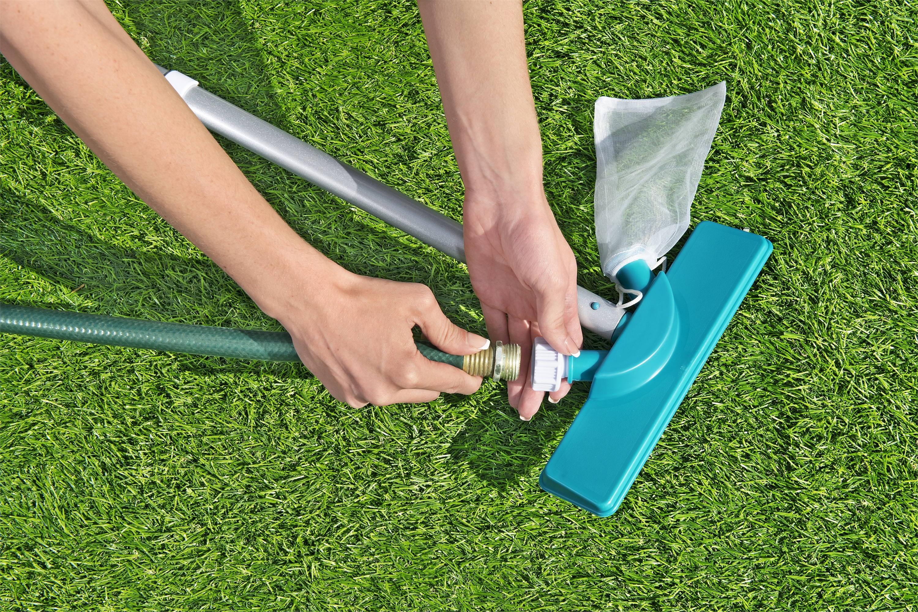Mani che collegano tubo da giardino a pulitore per piscina su erba sintetica.