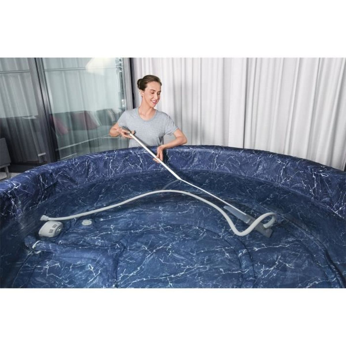 Una donna pulisce una piscina gonfiabile con un tubo e un pulitore.