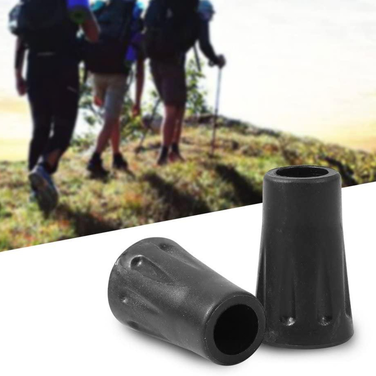 Due puntali neri per bastoncini da trekking su superficie bianca, escursionisti sfocati sullo sfondo.
