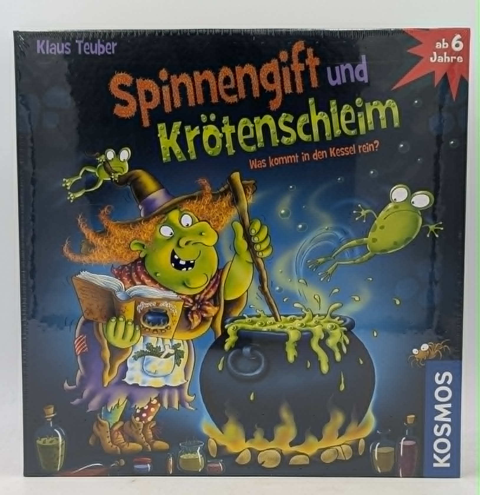 Grüne Hexe kocht in Kessel, Frösche springen. Brettspiel Spinnengift und Krötenschleim.