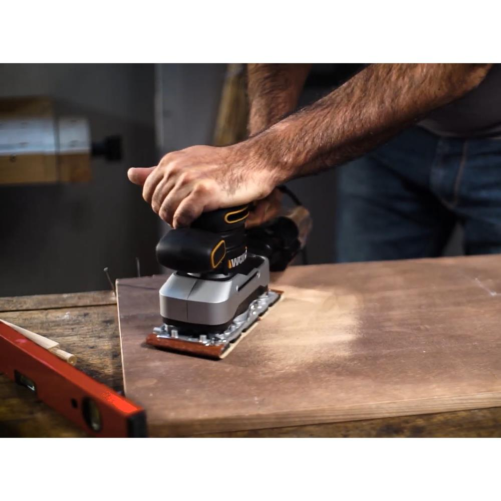Uomo leviga legno con levigatrice elettrica su banco da lavoro.