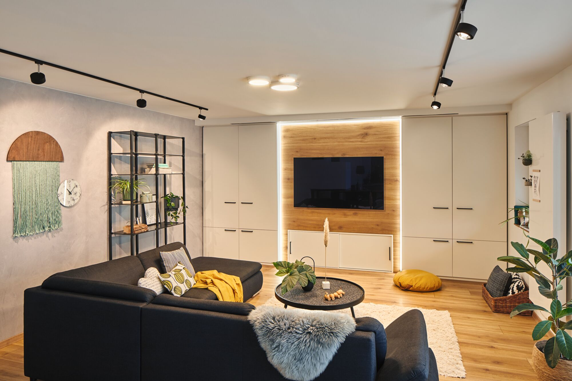 Modernes Wohnzimmer mit dunklem Sofa, Holzwand und Fernseher. Ein Regal steht links.