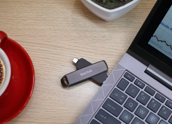 Ein USB-Stick von SanDisk liegt auf einem Laptop neben einer Kaffeetasse.