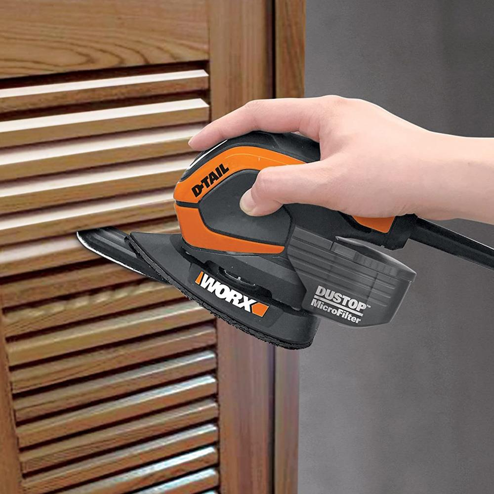 Una mano tiene una levigatrice arancione e nera utilizzata su un mobile in legno.