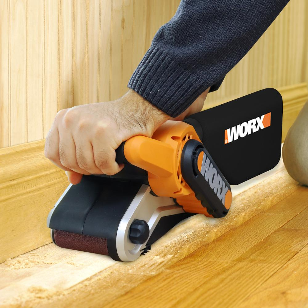 Ein Mann schleift einen Holzboden mit einem orangen und schwarzen Schleifgerät von Worx.