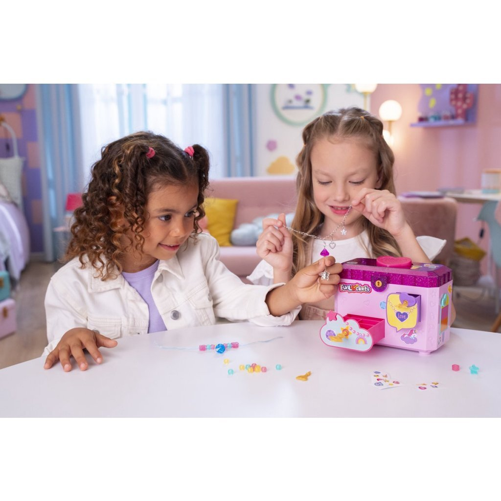 Dos niñas hacen joyas en una mesa con una máquina de joyas rosa.