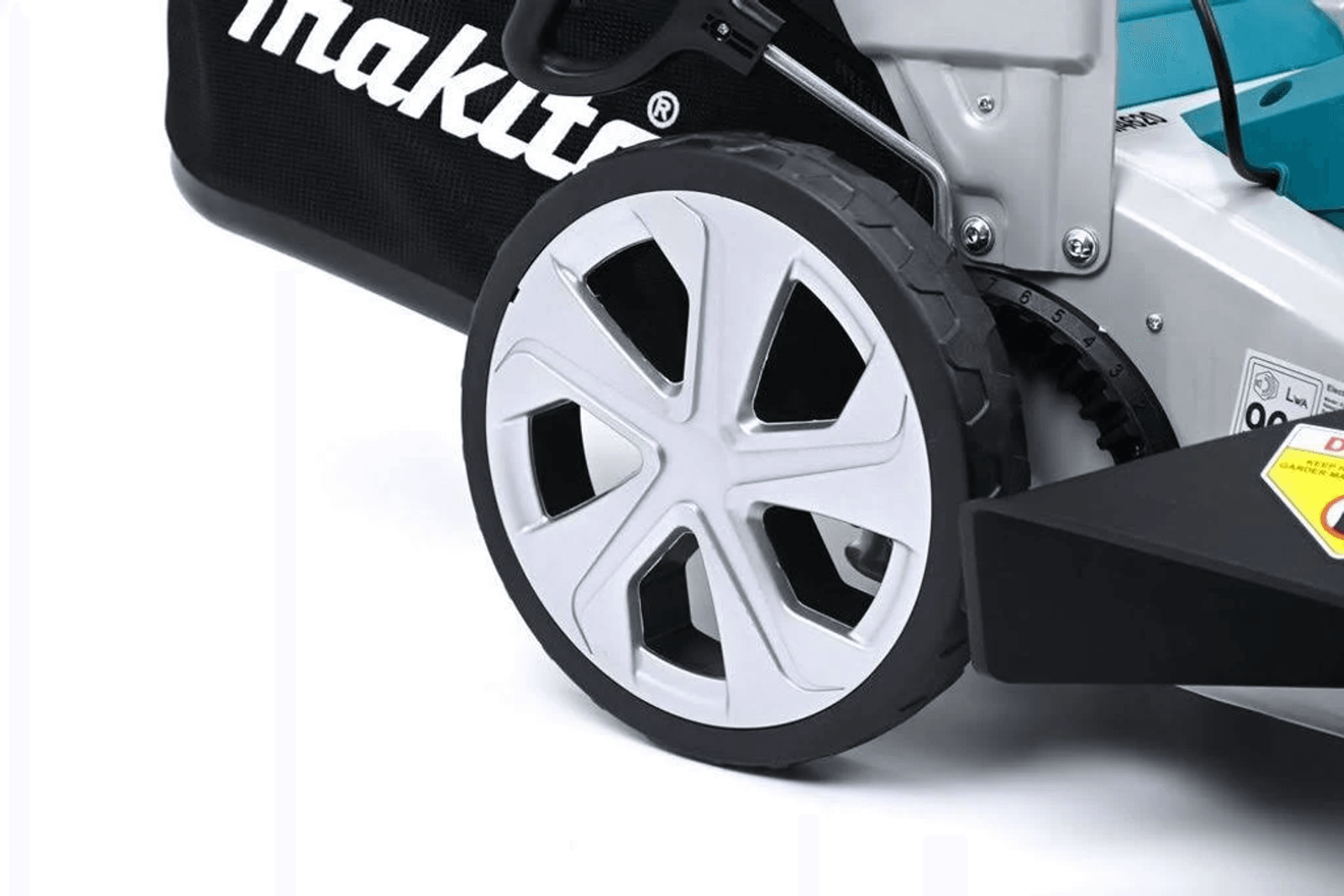 Primer plano de la rueda de un cortacésped con radios plateados y neumático negro. Logo Makita en bolsa negra.