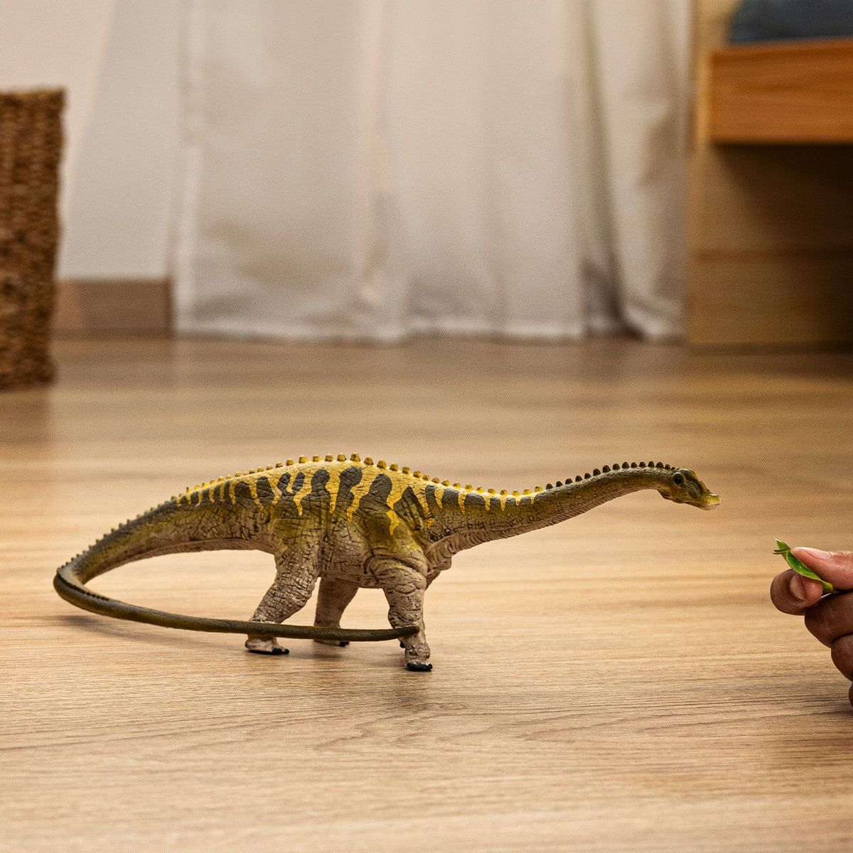 Ein Dino-Spielzeug streckt seinen Hals zu einer Hand, die etwas Grünes hält.