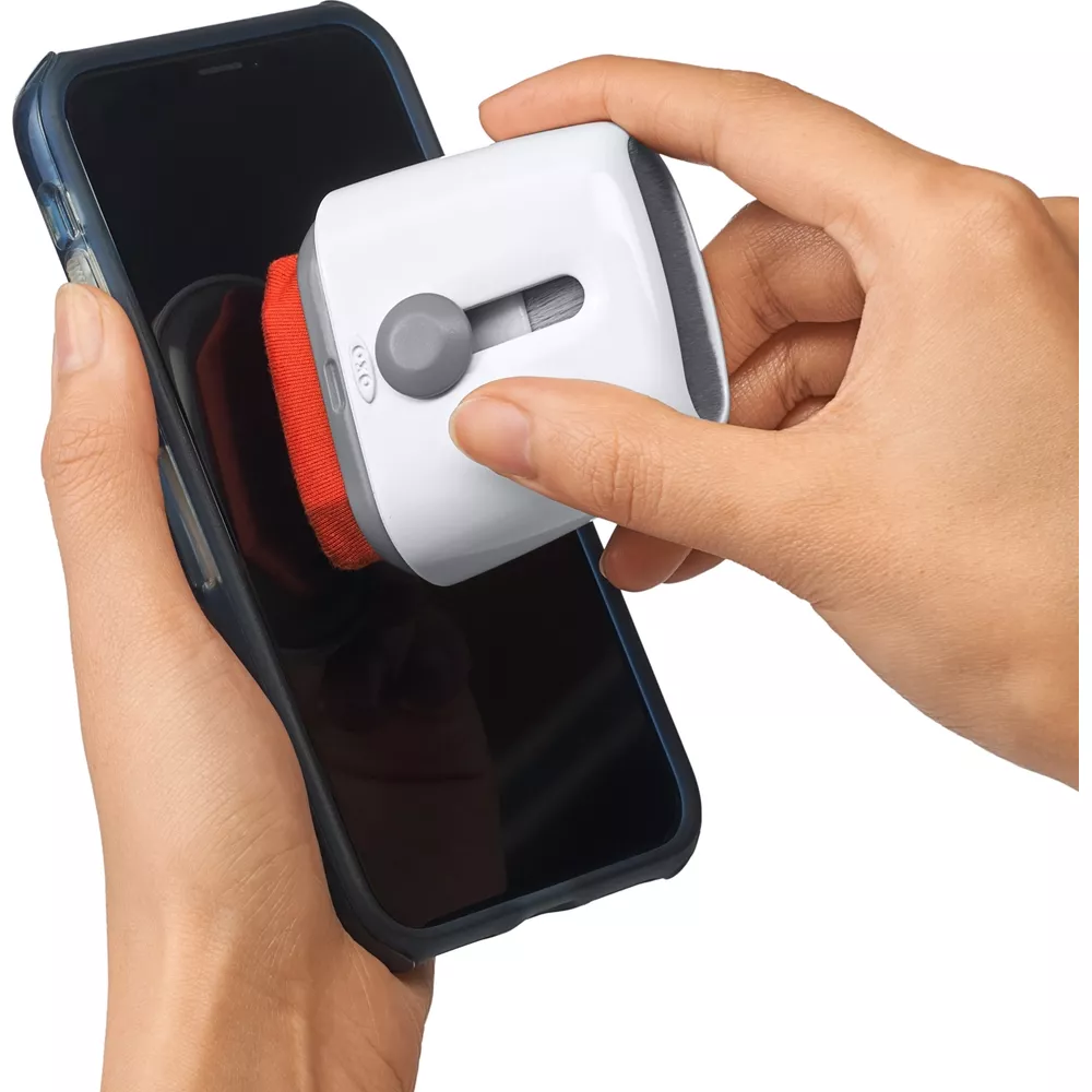 Eine Hand hält ein Smartphone, während eine andere Hand einen weißen Reiniger mit rotem Pad benutzt.