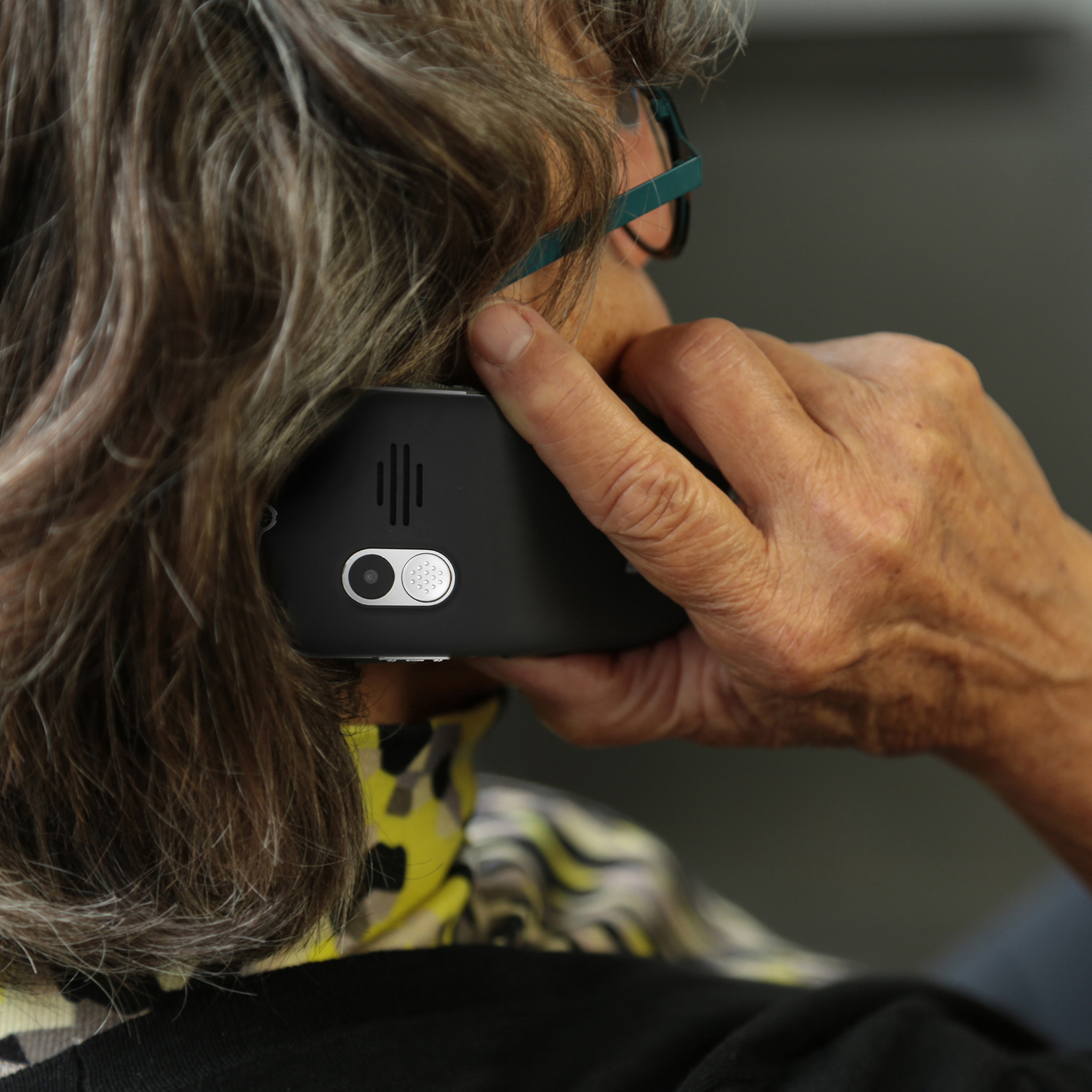 Eine Person mit grauem Haar telefoniert mit einem schwarzen Smartphone.