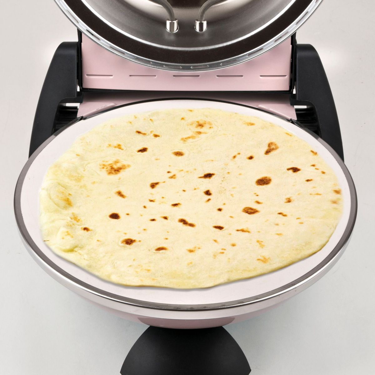 Una piadina chiara con macchie marroni su una superficie di cottura rotonda.