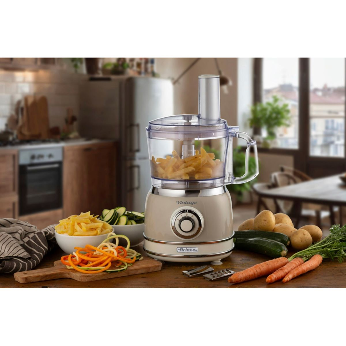 Food processor beige con zucchine, carote e patate su tavolo di legno.