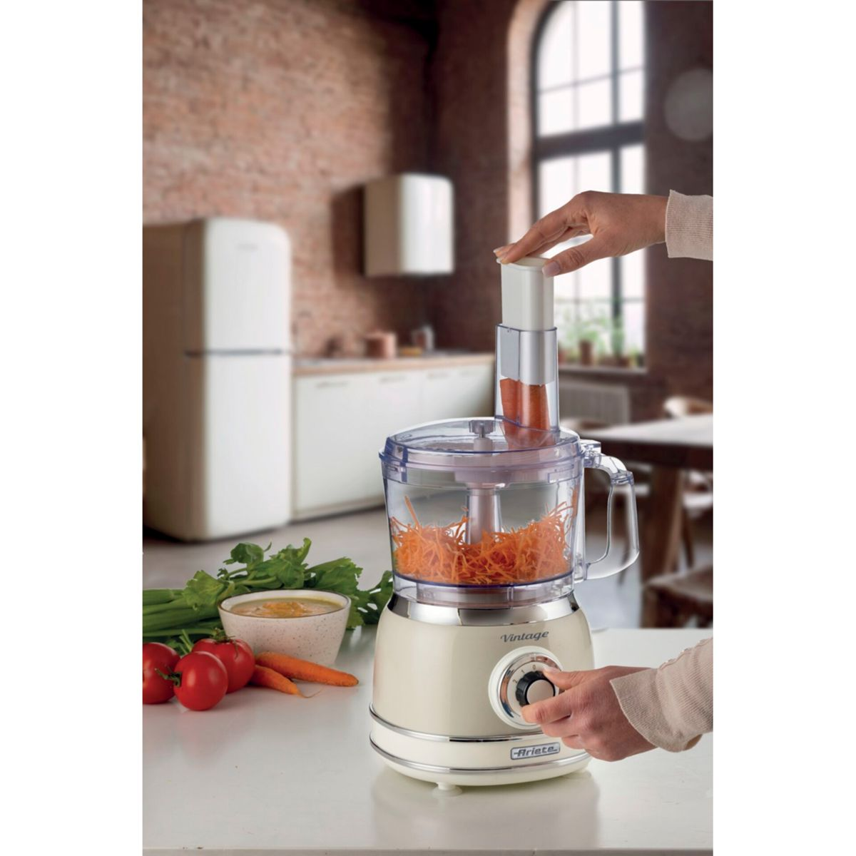 Una persona usa un robot da cucina beige per grattugiare carote.