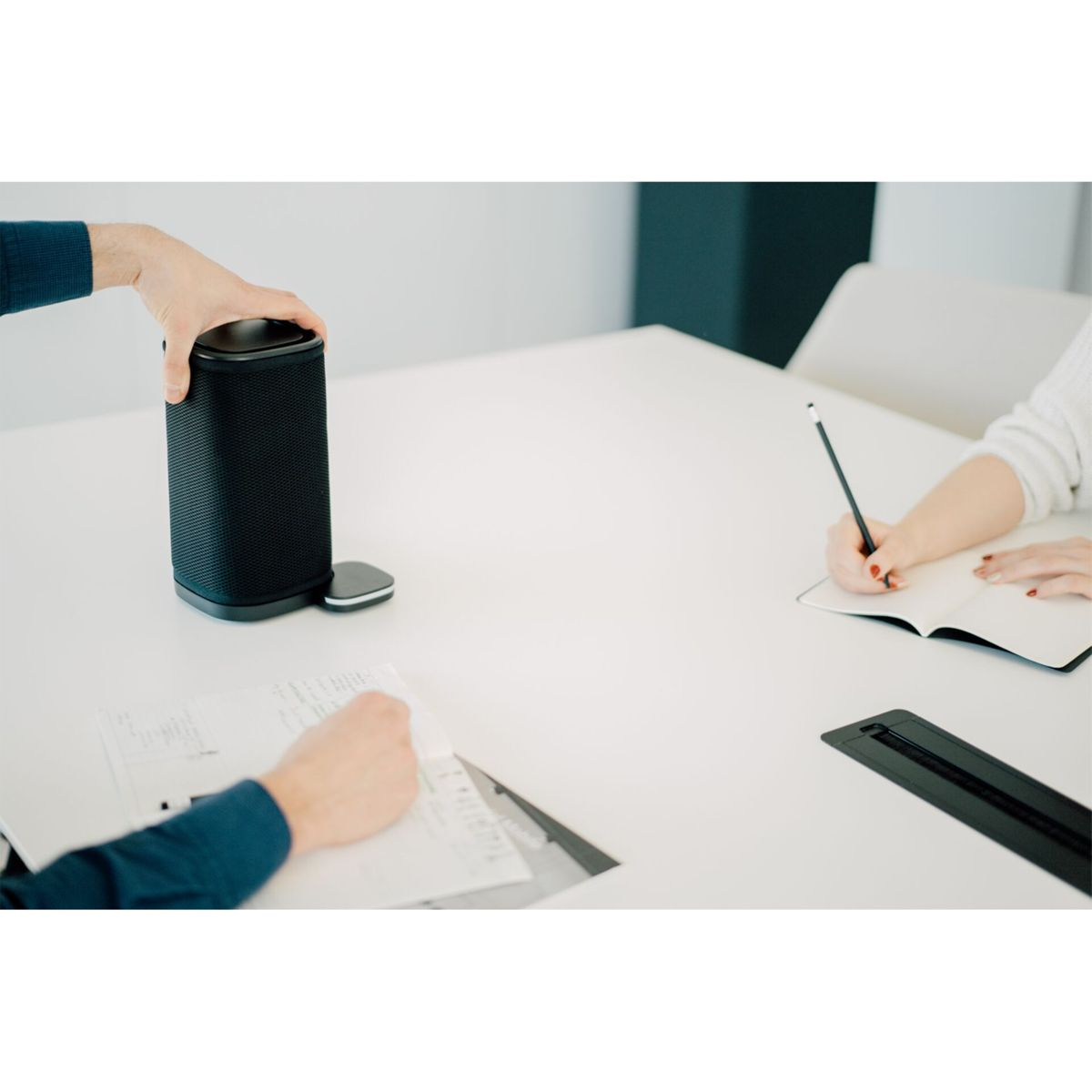 Personen in einem Meeting: Einer bedient einen Lautsprecher, ein anderer schreibt.