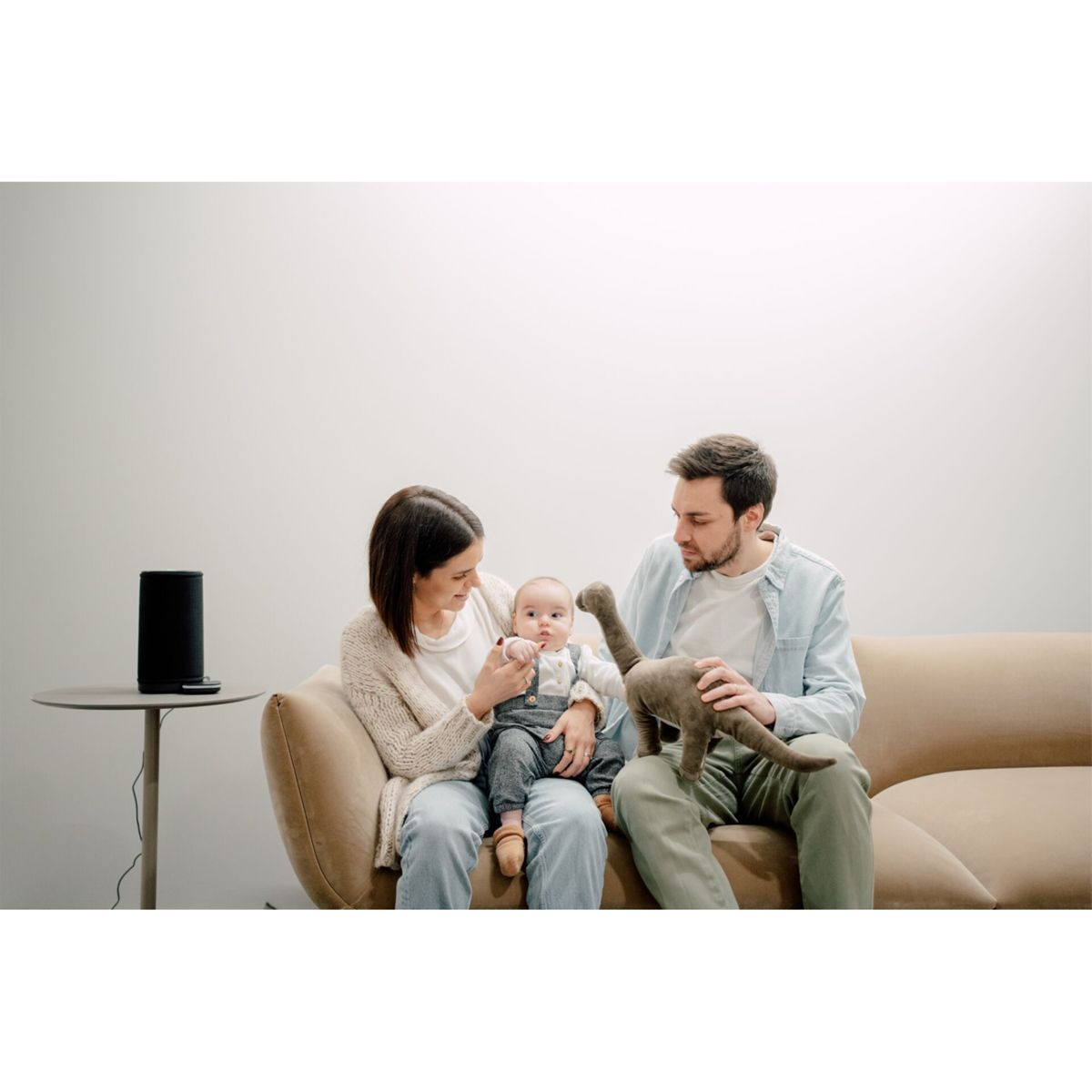 Familie auf Sofa mit Baby und Spielzeug Dino, Lautsprecher auf Tisch.