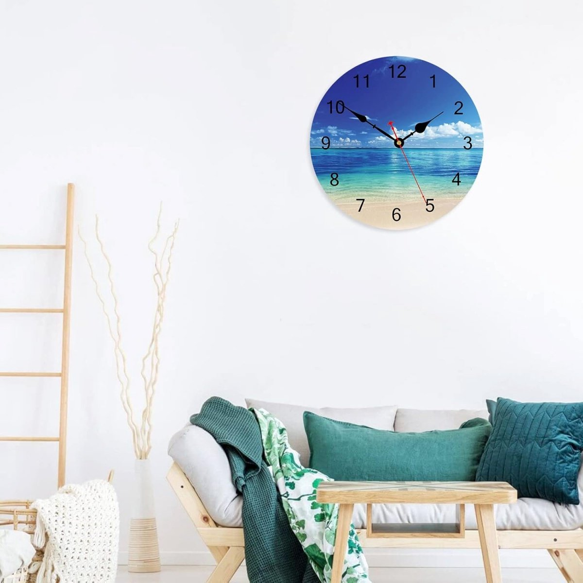 Eine Wanduhr mit einem tropischen Strandmotiv hängt an einer weißen Wand über einem Sofa.