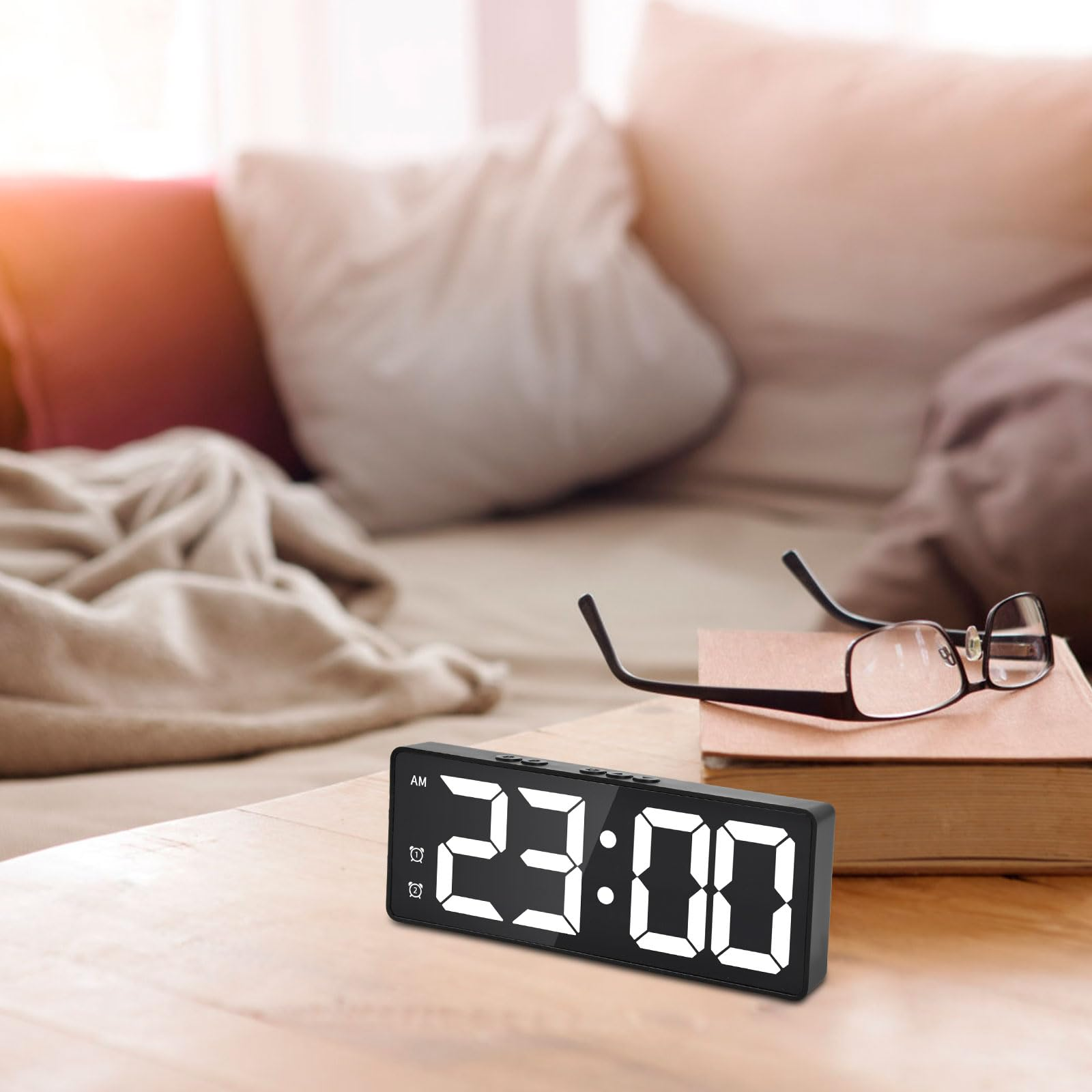 Eine Digitaluhr zeigt 23:00 Uhr an. Eine Brille liegt daneben auf einem Buch auf einem Holztisch.