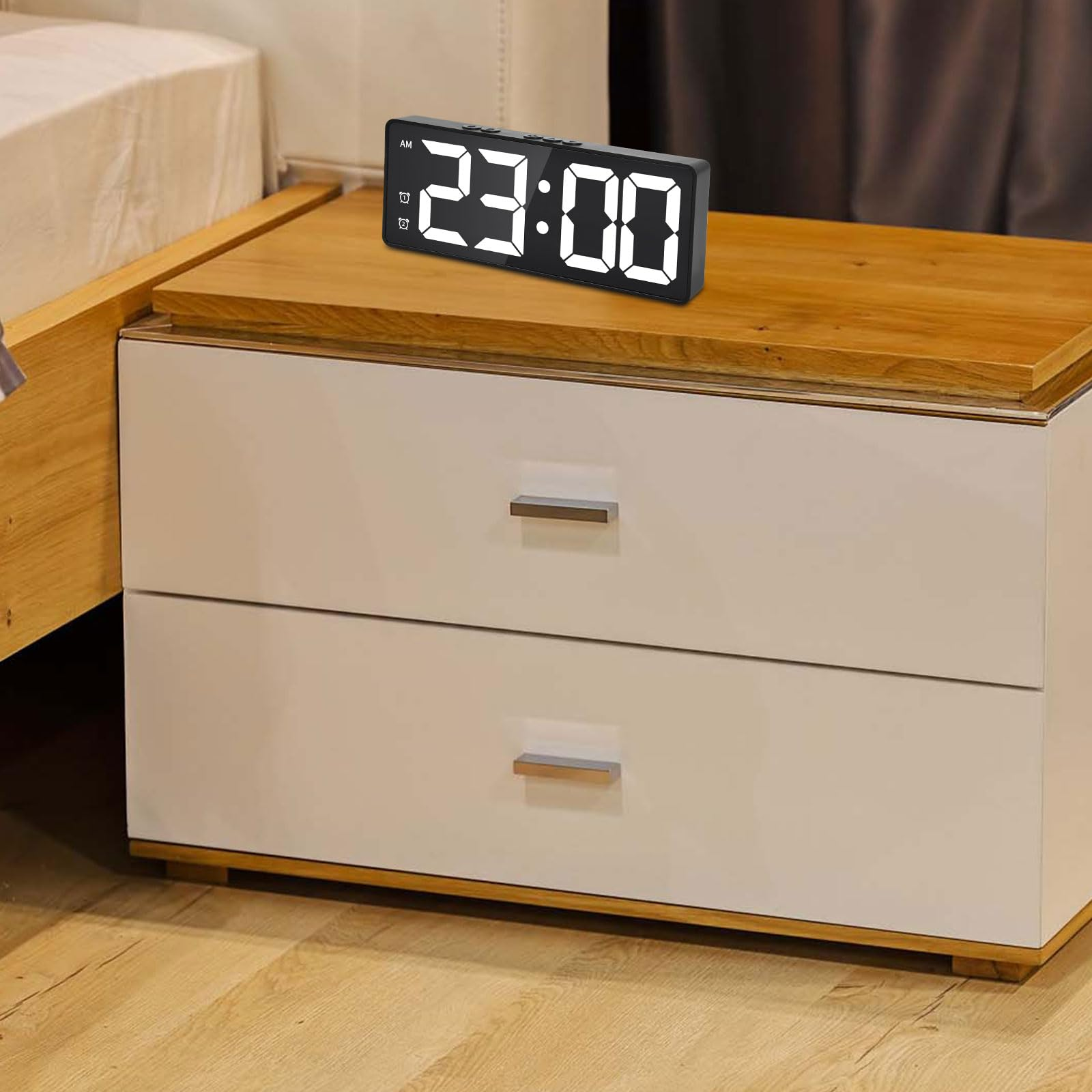Ein schwarzer Digitalwecker zeigt 23:00 auf einem Nachttisch neben einem Bett.