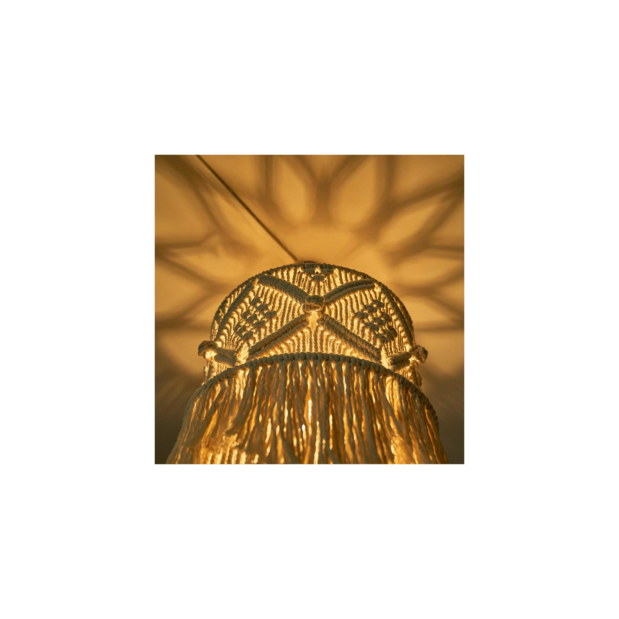 Eine Makramee-Lampe wirft ein sternförmiges Lichtmuster an die Wand.