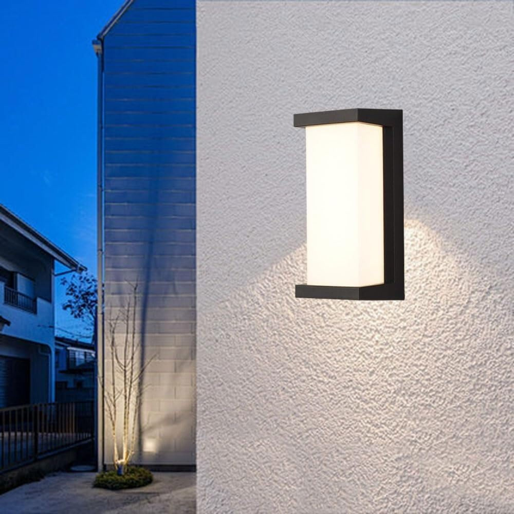 Ein moderner Wandleuchter beleuchtet eine weiße Hauswand. Im Hintergrund ist ein Haus.