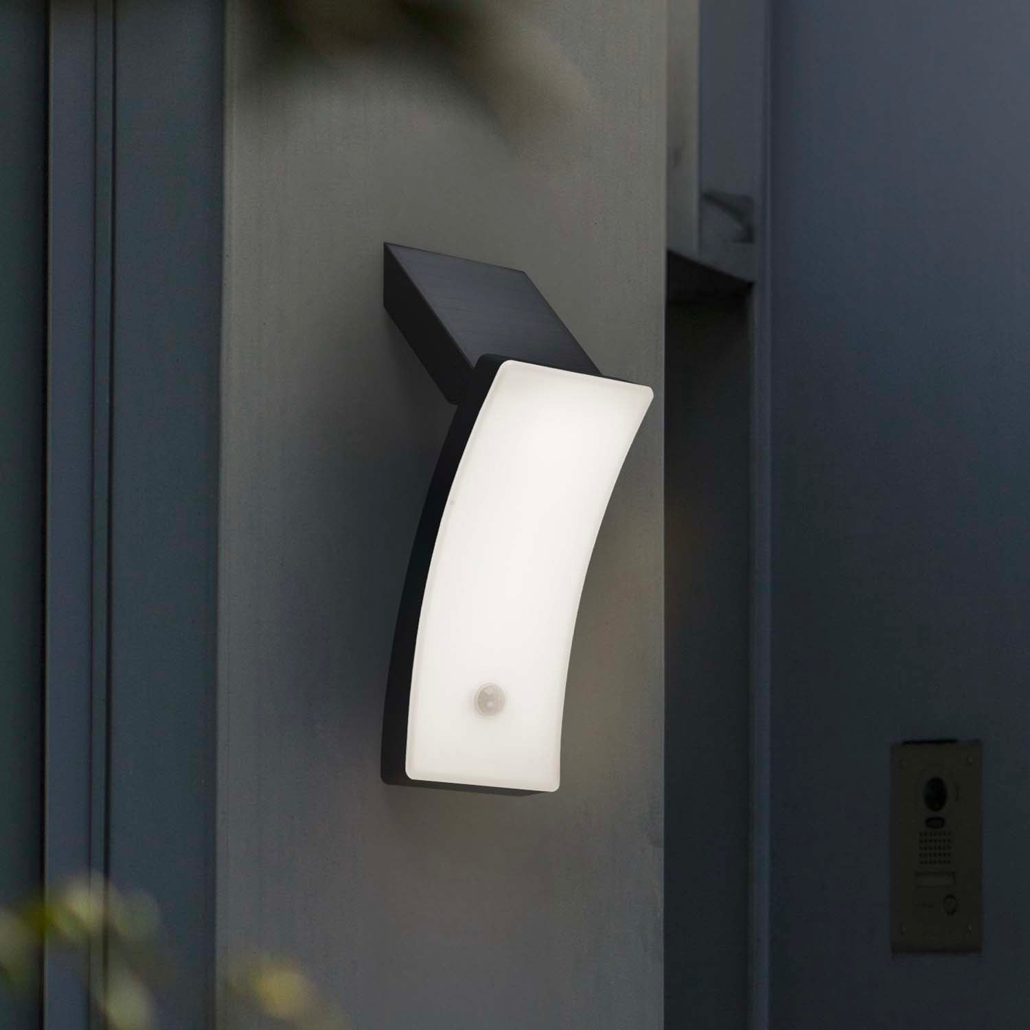 Moderne weiße Wandleuchte mit Bewegungsmelder an grauer Wand, neben einer Klingelanlage.