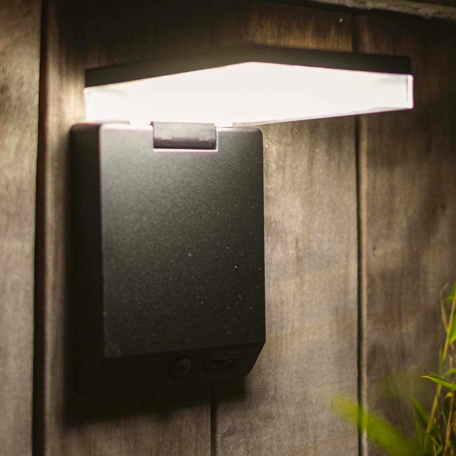 Eine moderne schwarze Wandleuchte mit einem rechteckigen Lichtelement leuchtet hell.