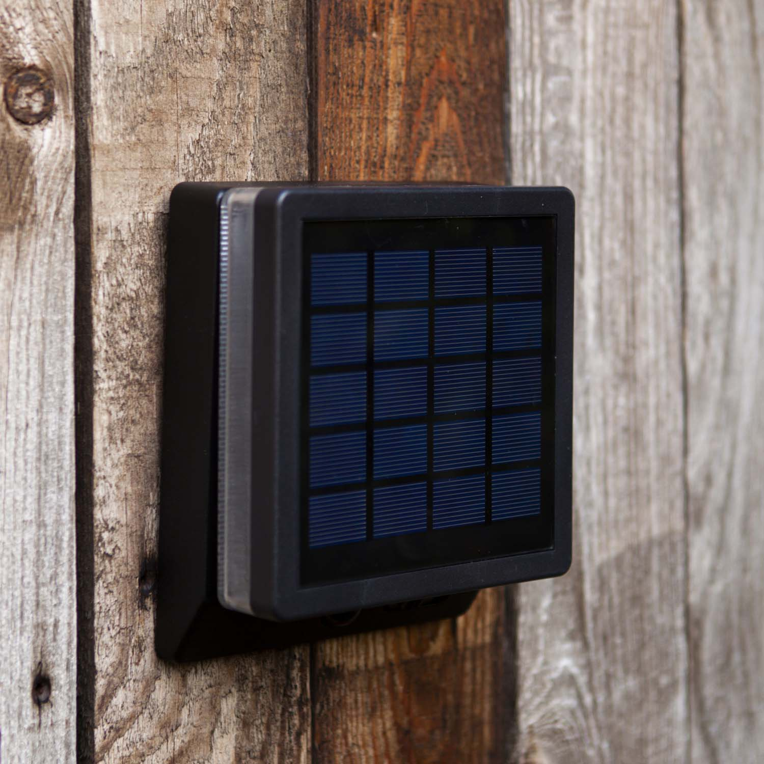 Ein schwarzes Solarpanel mit blauen Zellen ist an einer Holzwand befestigt.