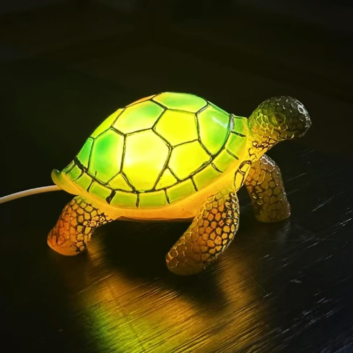 Eine leuchtende Schildkrötenlampe mit grün-gelbem Panzer auf dunklem Hintergrund.