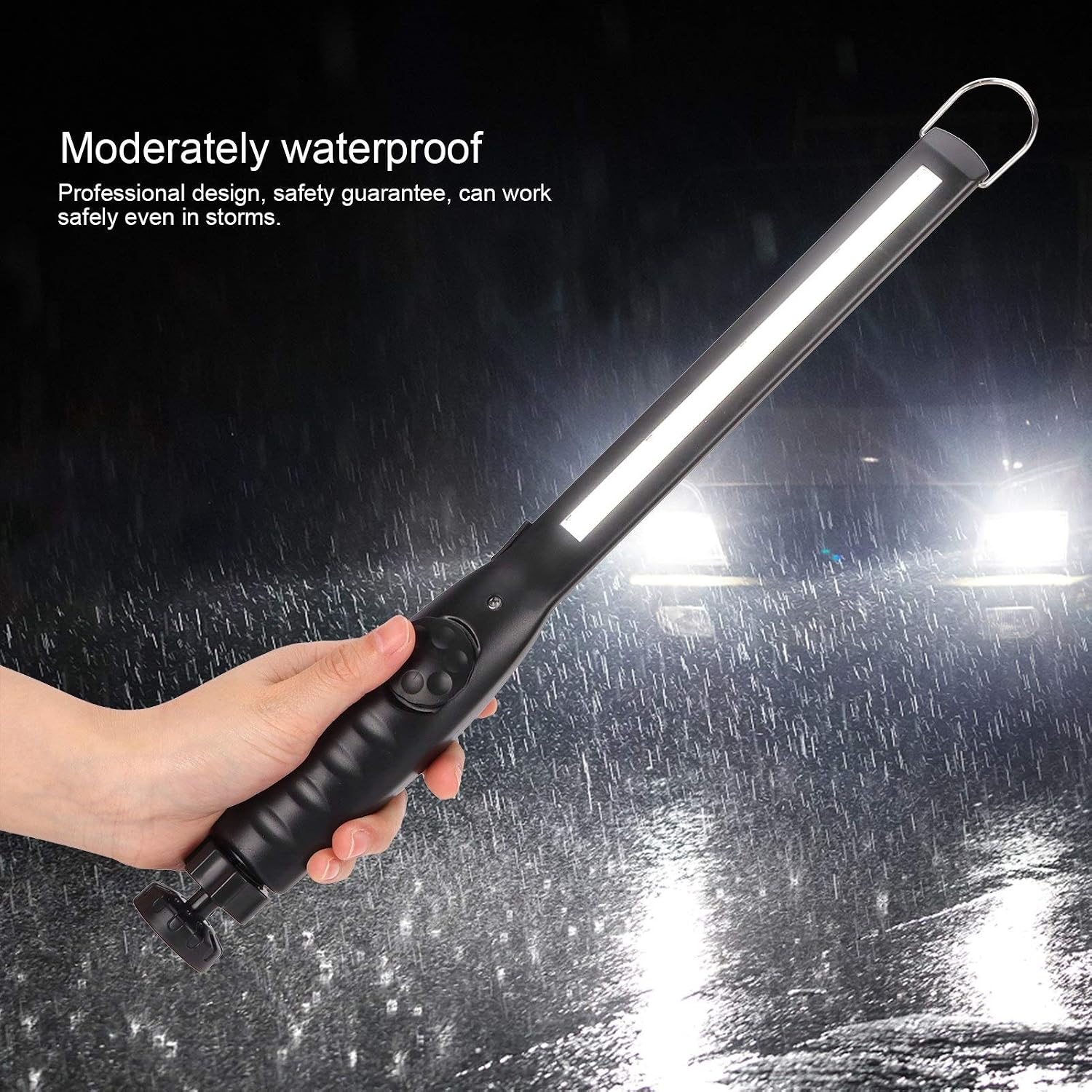 Eine Hand hält eine schwarze LED-Arbeitsleuchte bei einem Regensturm, im Hintergrund helle Scheinwerfer.