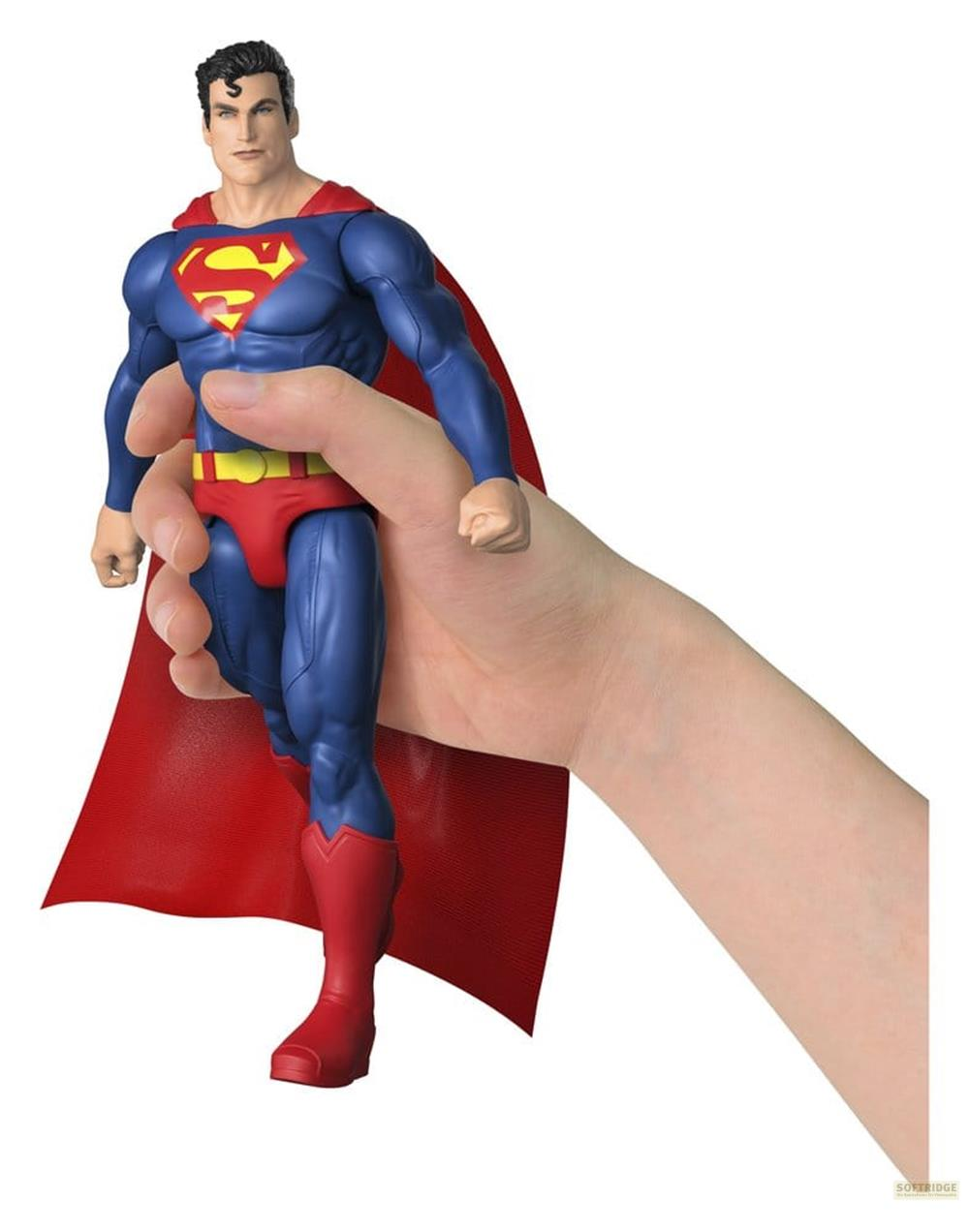 Figura de Superman en mano, traje azul, capa roja, fondo blanco.