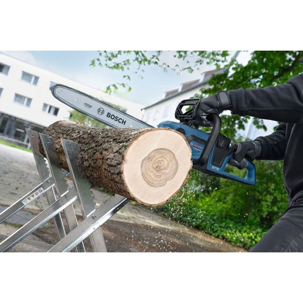 Eine Person schneidet mit einer blauen Kettensäge einen Holzstamm auf einem Sägebock.