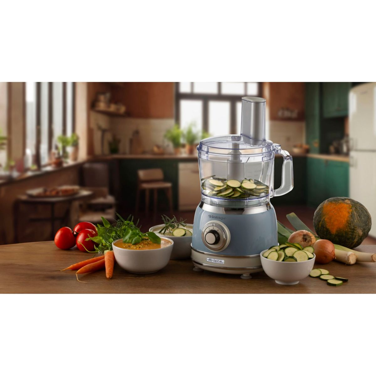Un robot da cucina blu con zucchine affettate e verdure su tavolo in legno.