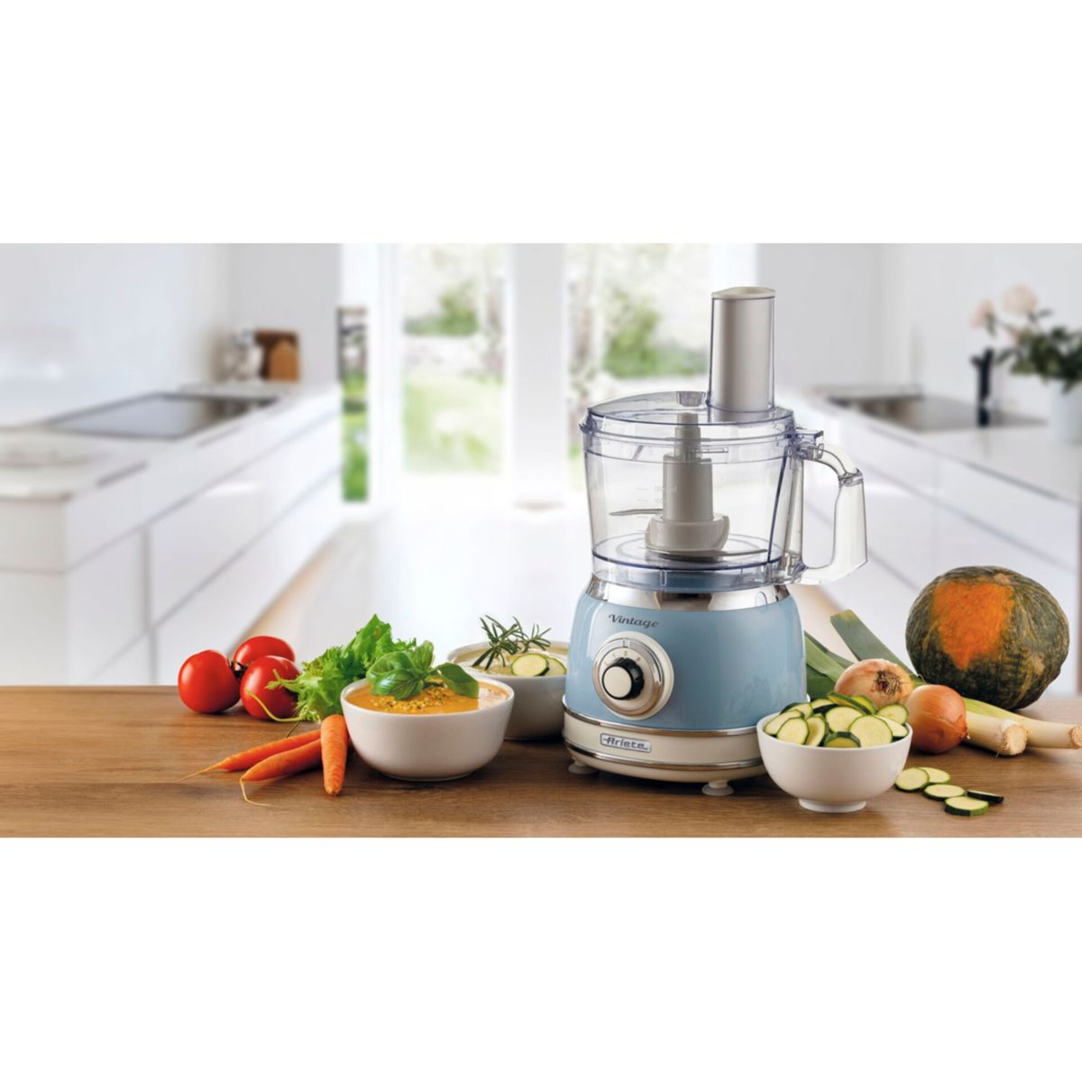 Un robot da cucina blu su un tavolo di legno con verdure come carote, pomodori e zucchine.