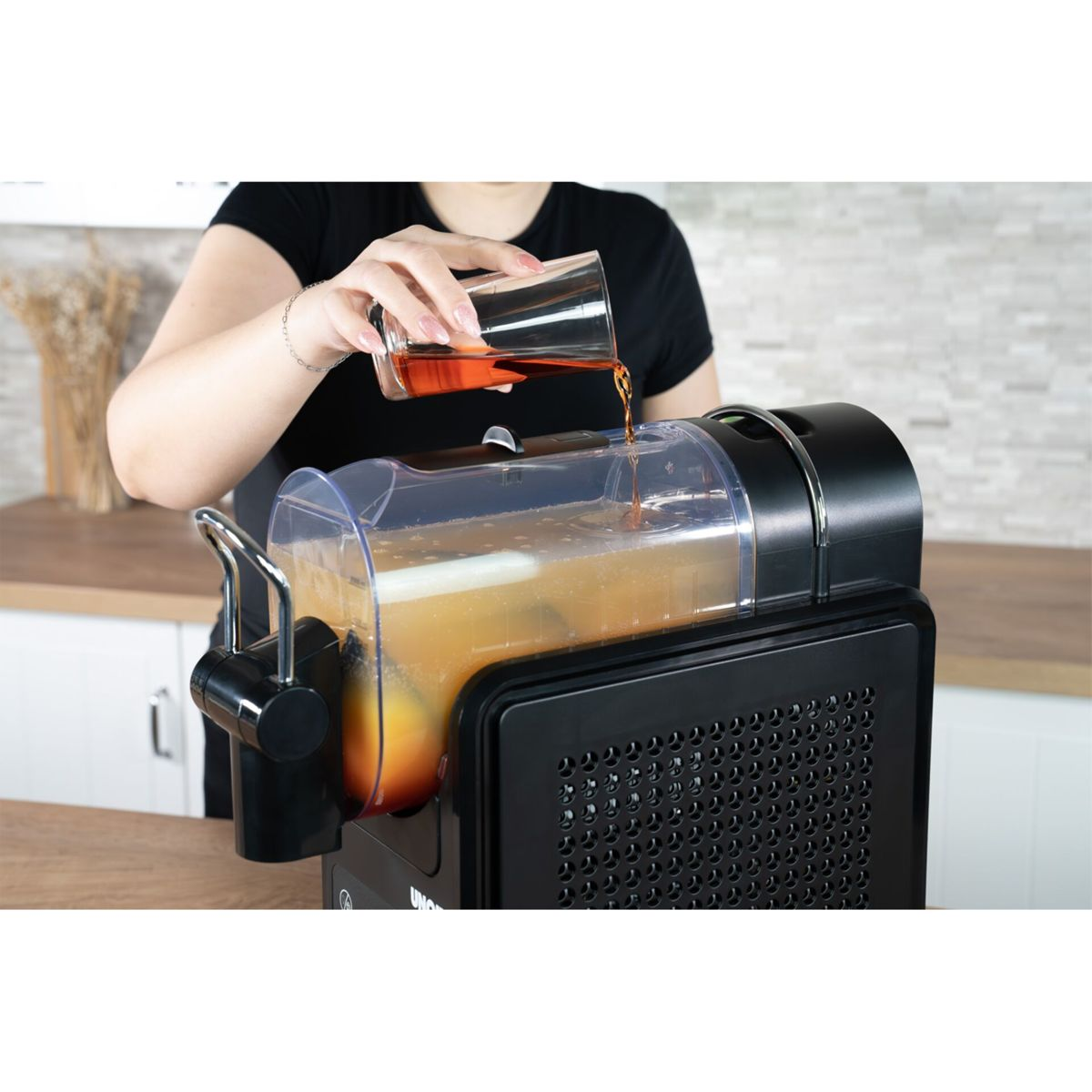 Una persona versa liquido marrone da un bicchiere in un distributore di bevande.