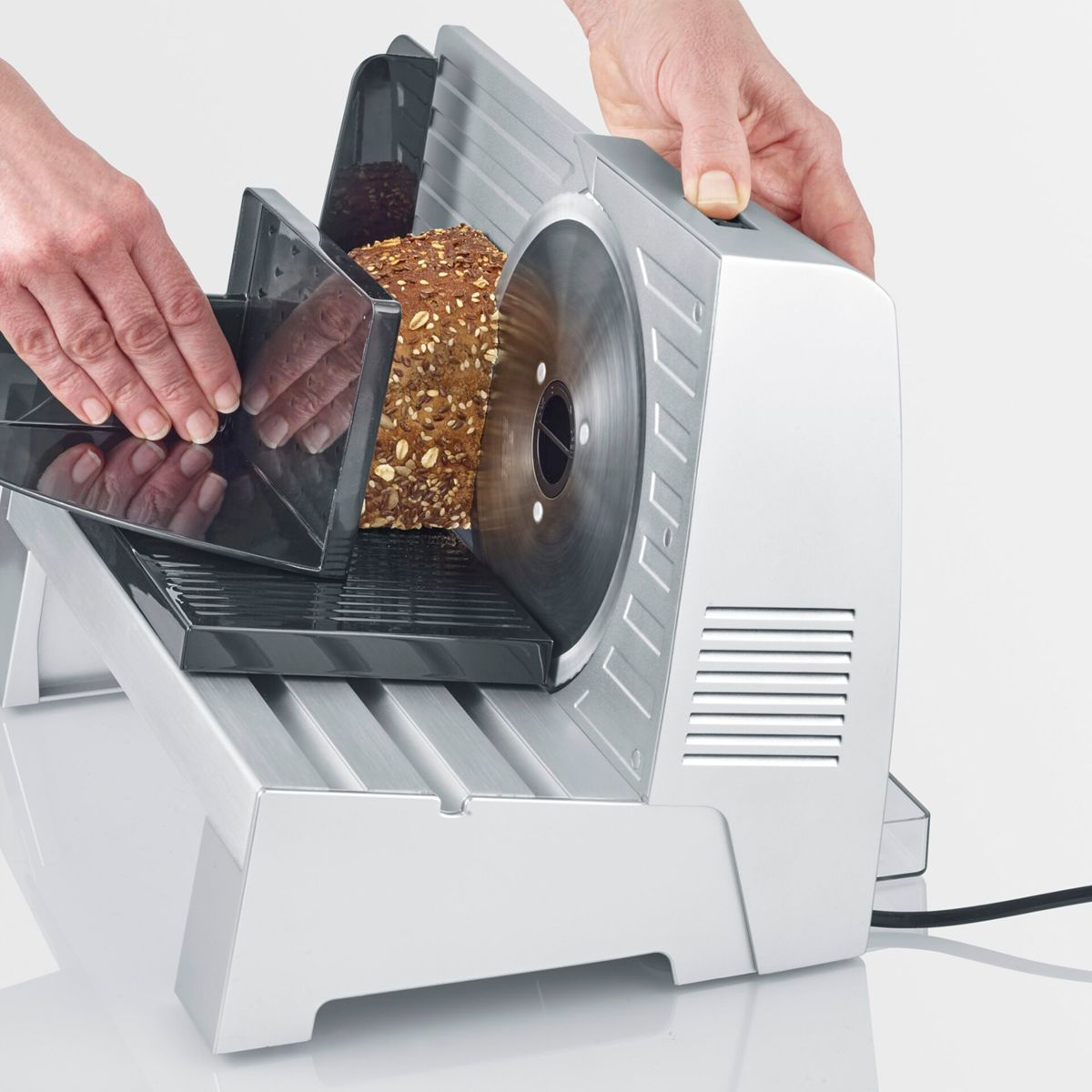 Hände führen Brot in einen elektrischen Brotschneider mit einer runden Klinge.