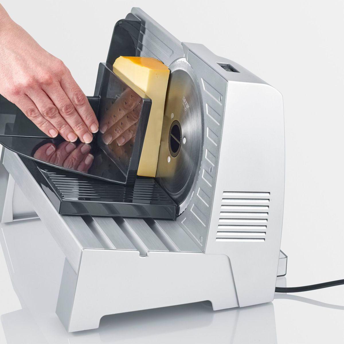 Eine Hand schiebt ein Stück Käse in einen elektrischen Schneider.