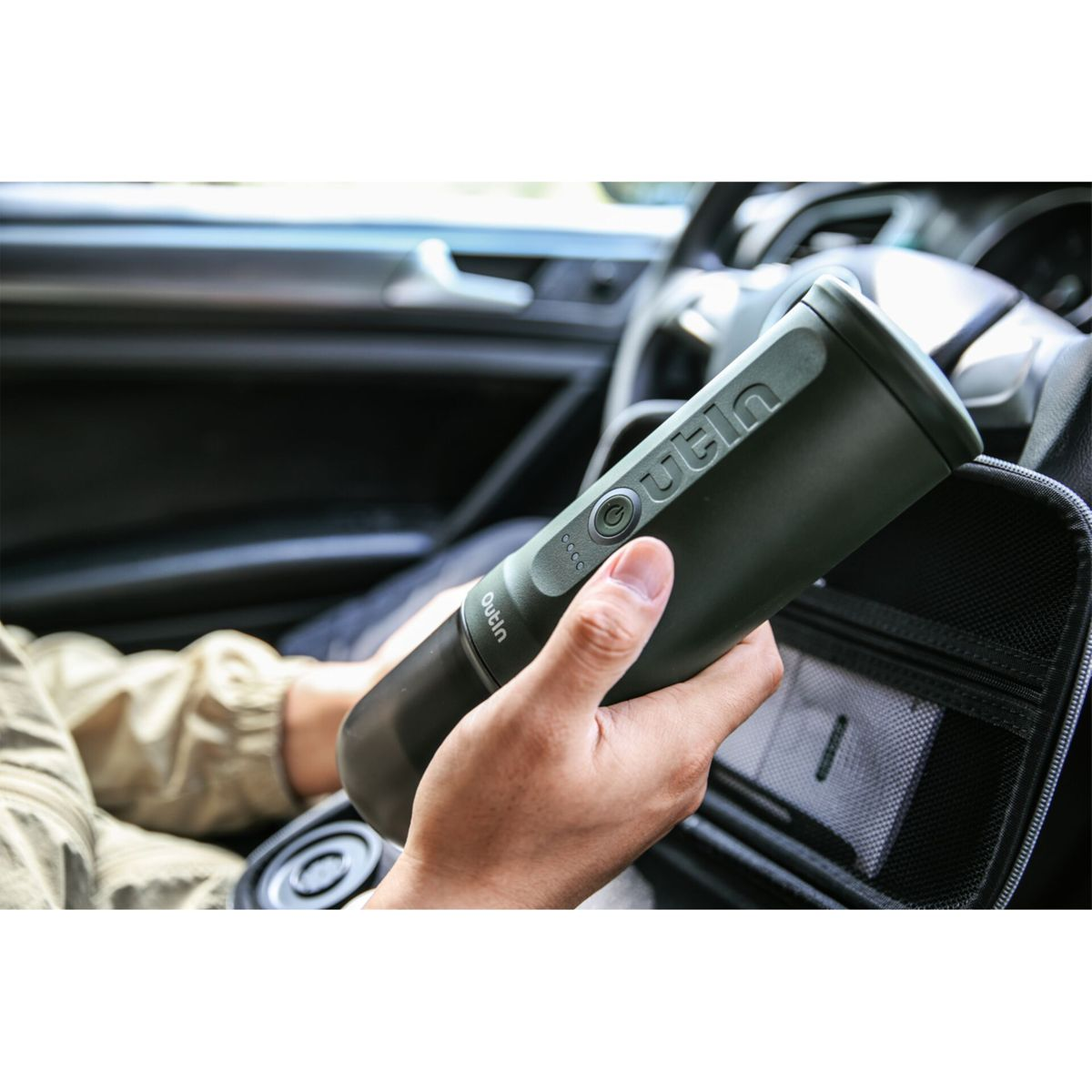 Una persona tiene un filtro per l'acqua Outin verde scuro in un'auto, con una custodia nelle vicinanze.