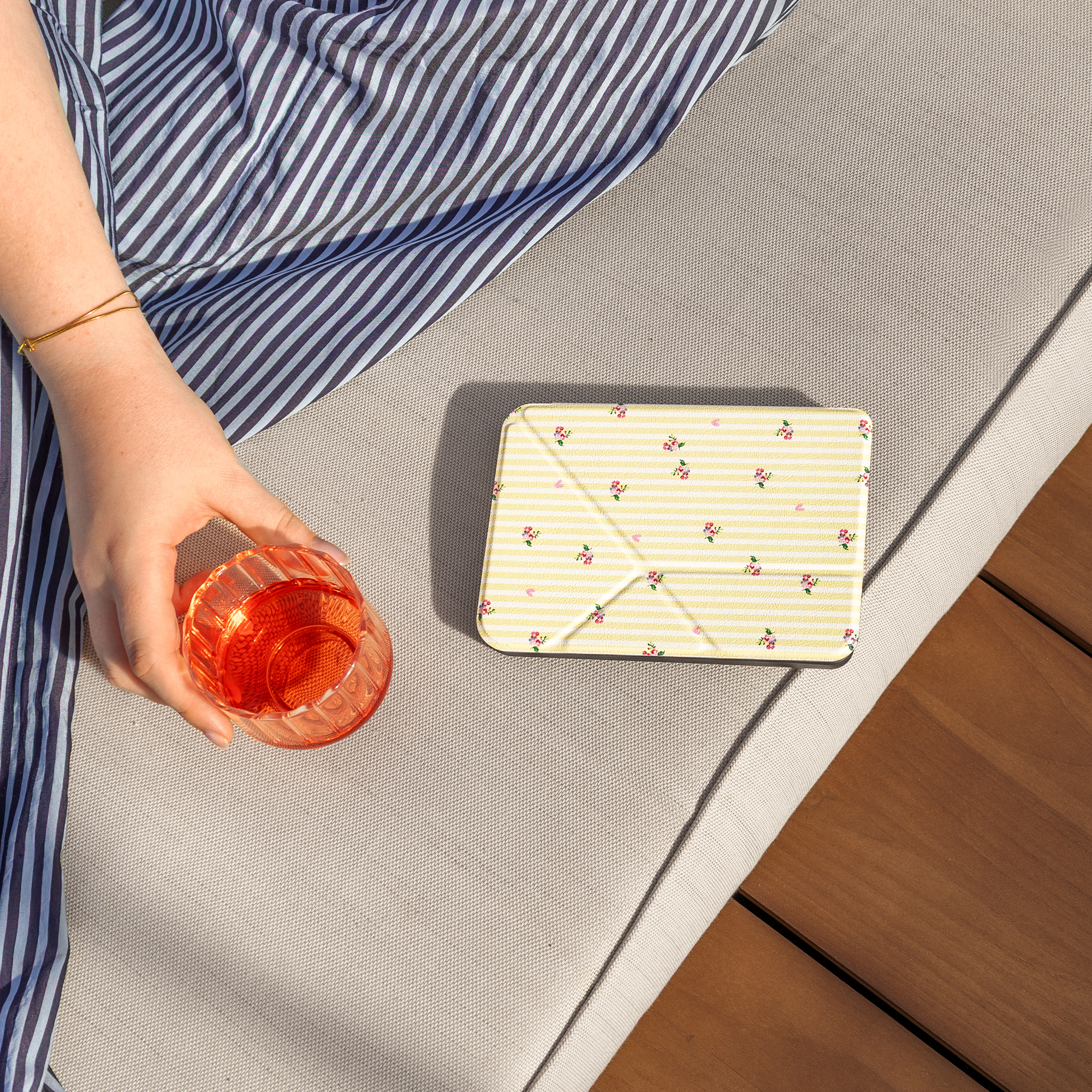 A hand holds a glass of red drink next to a yellow floral patterned case.