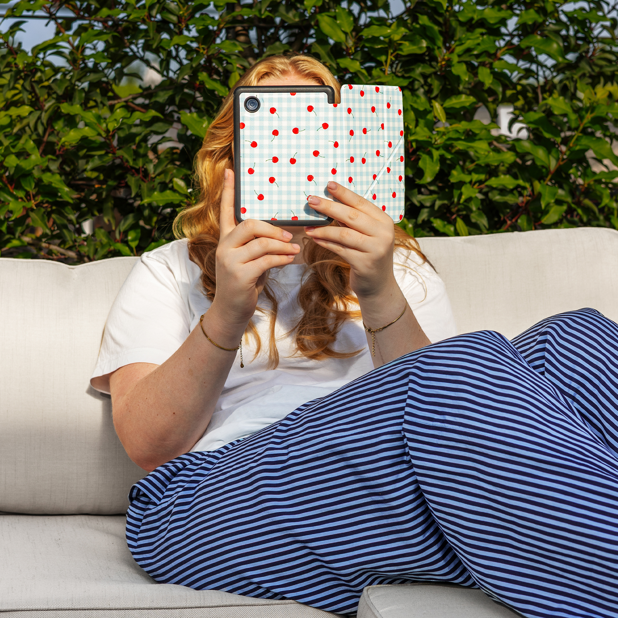 A person sits on a couch holding a tablet with a cherry pattern.