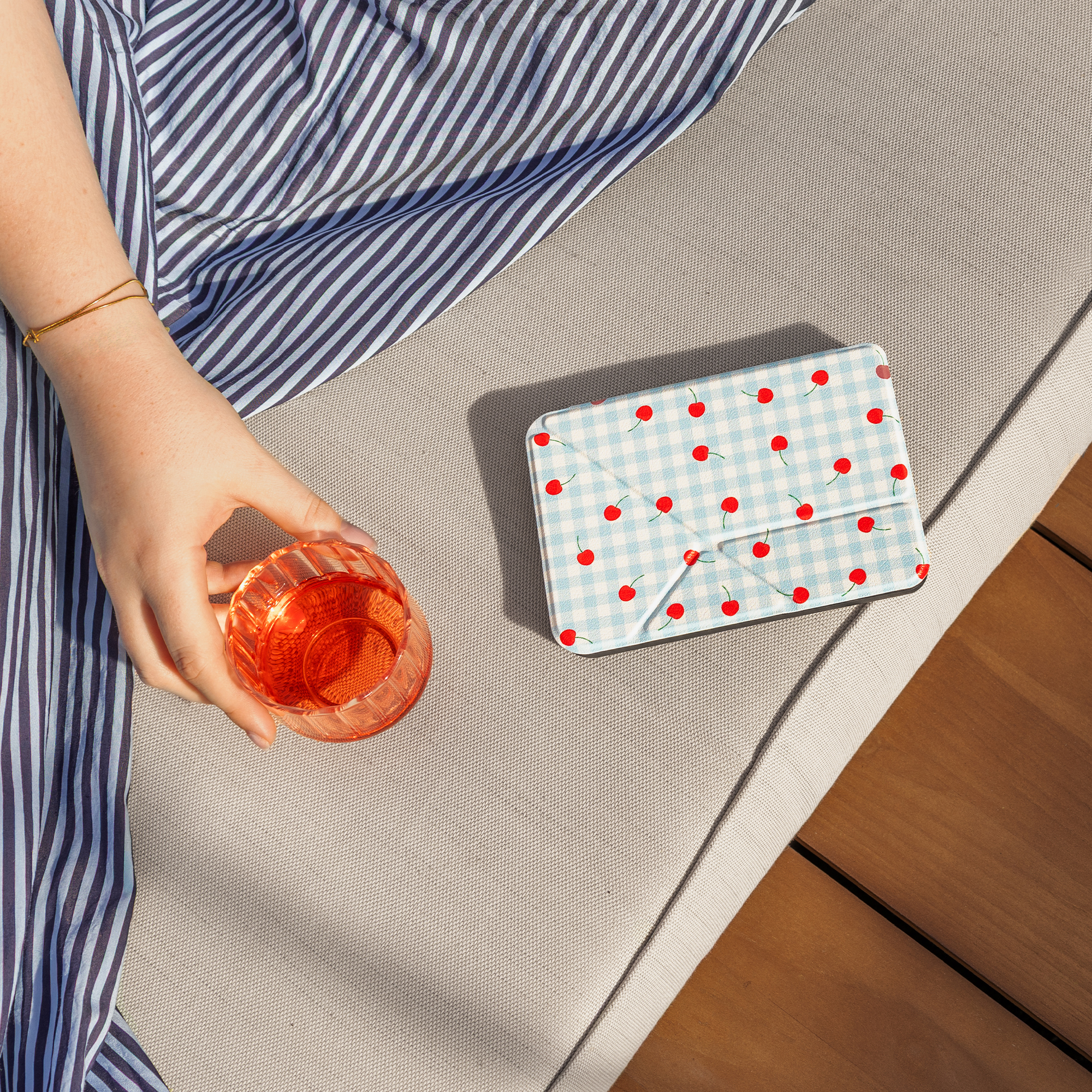 A hand holds a glass of pink drink next to a cherry-patterned blanket.