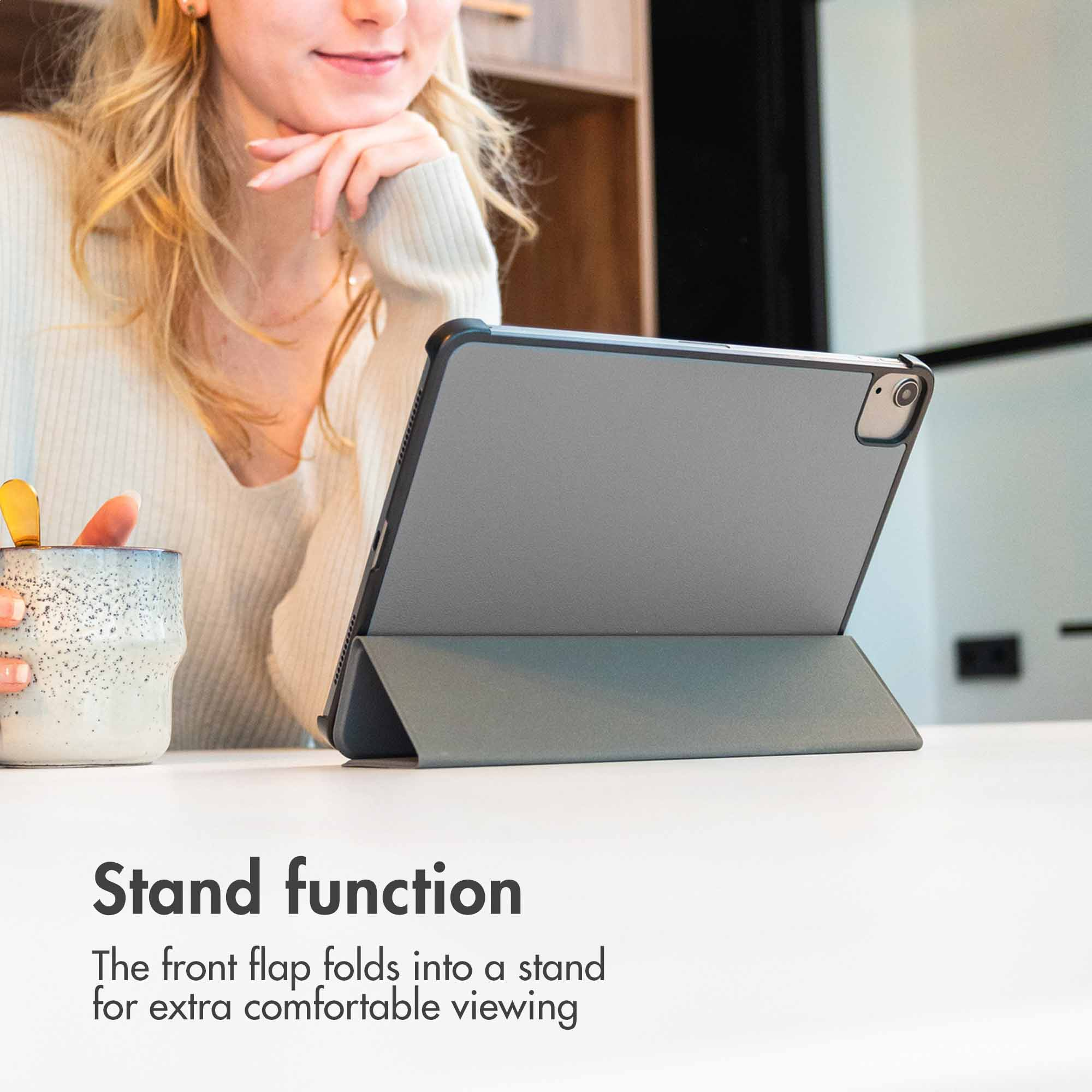 A woman holds a mug, a tablet stands on the table.