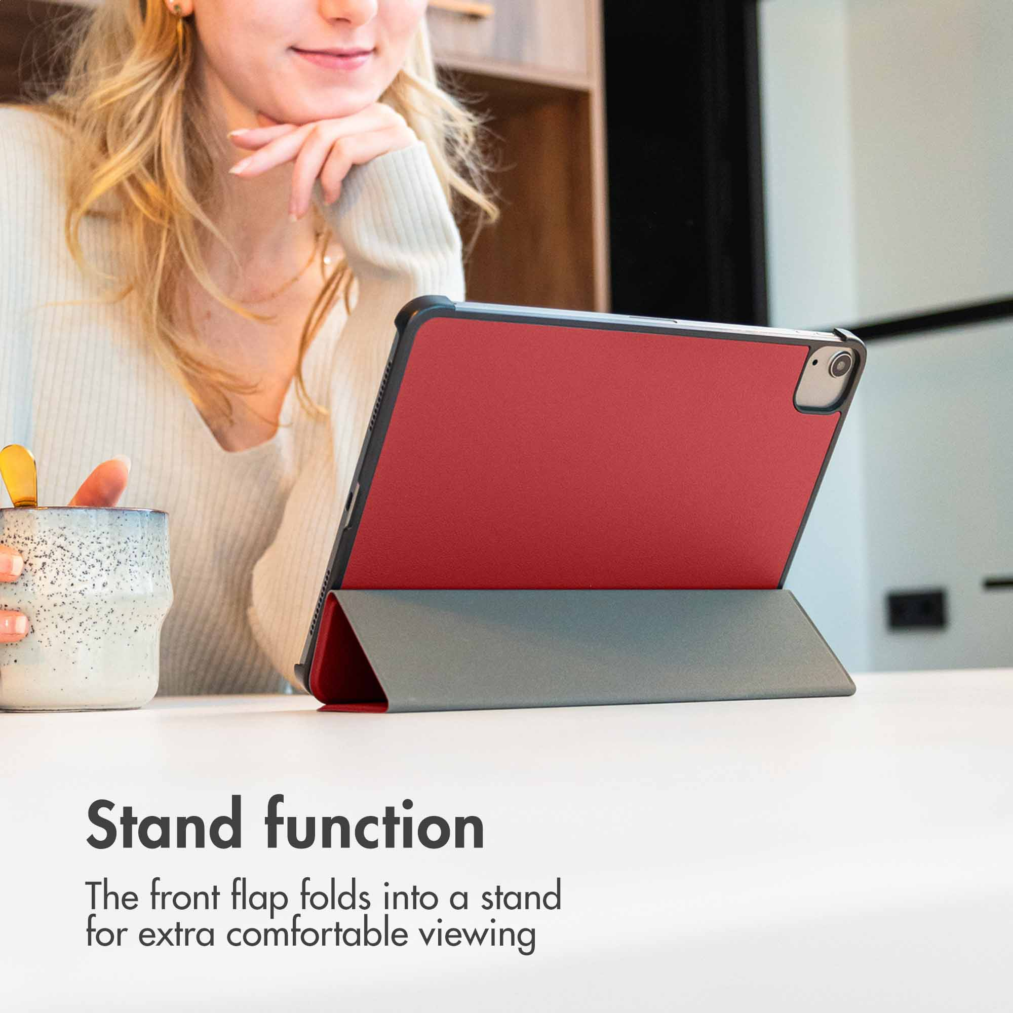 A woman sips from a speckled mug while a red tablet case with a stand function is positioned on a white table.