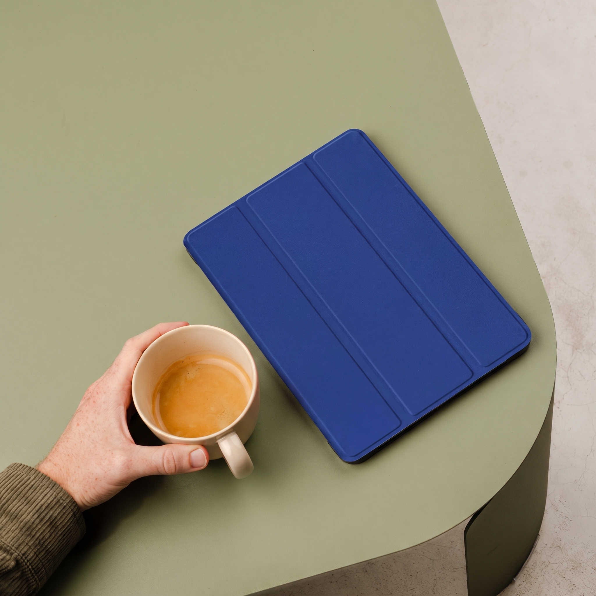A hand holds a coffee cup next to a blue tablet case on a table.