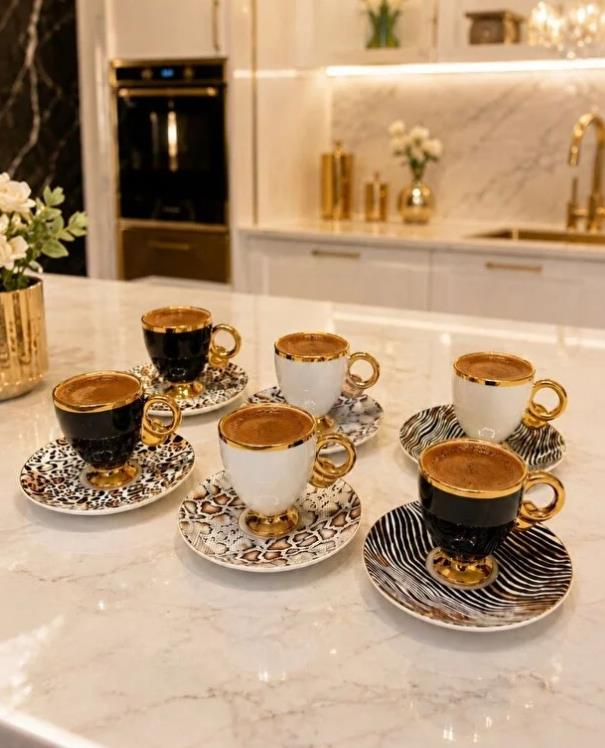 Altın kulplu altı kahve fincanı, desenli fincan tabaklarında, kahve dolu.