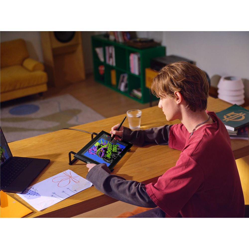 Ein Junge sitzt an einem Holztisch und zeichnet auf einem Tablet mit einem Stift.