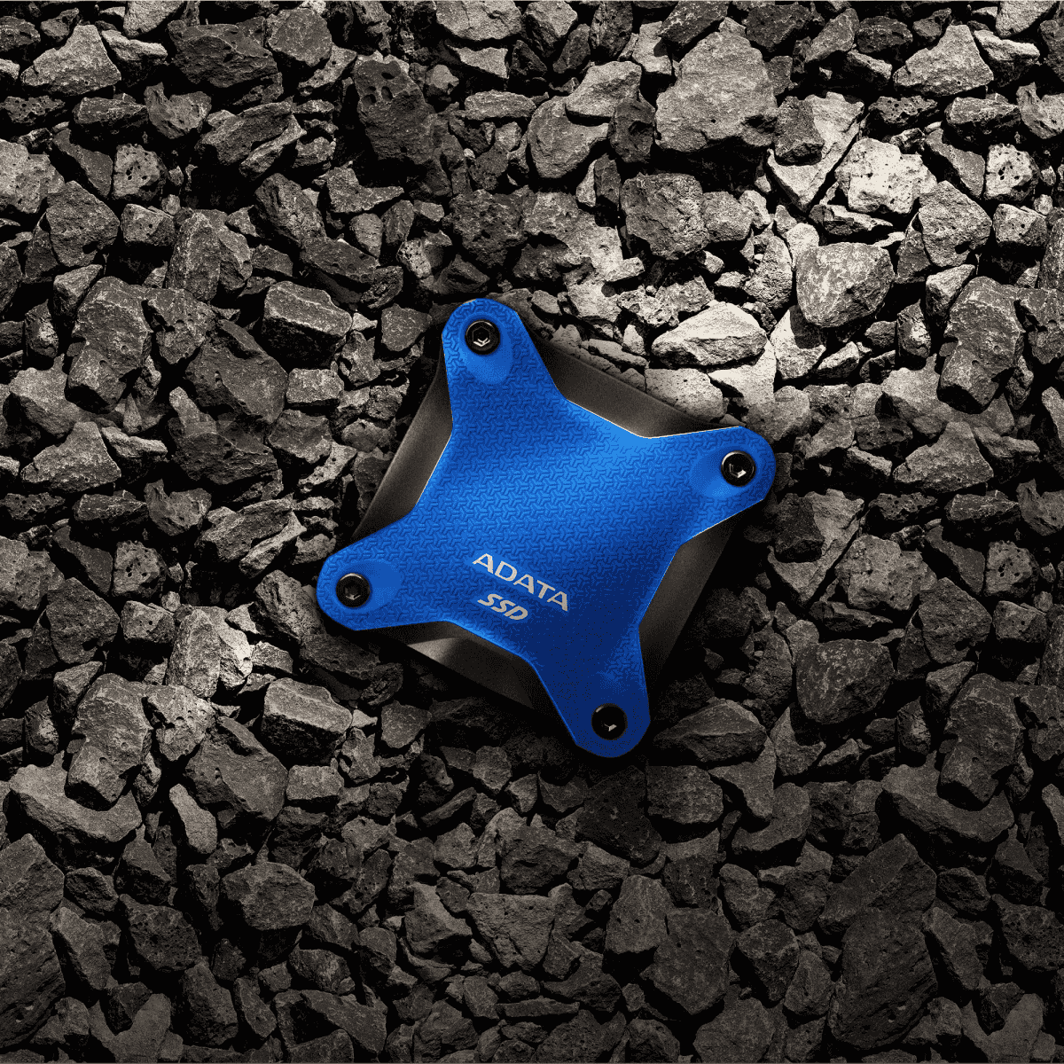 Un disco SSD ADATA azul descansa sobre un montón de rocas oscuras.
