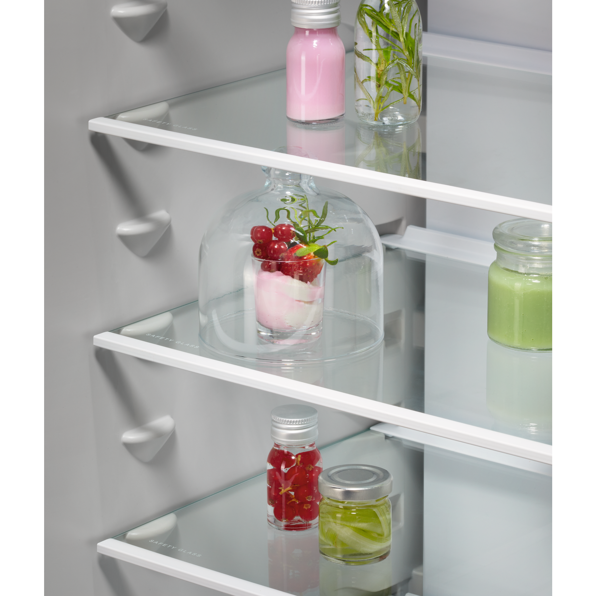Dentro del refrigerador: postre con bayas bajo cristal, líquidos verdes y rojos en frascos.