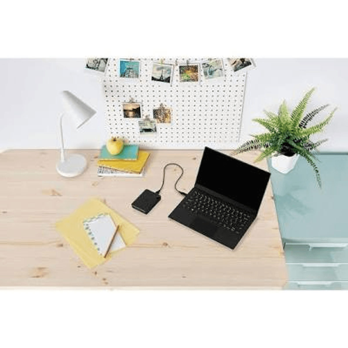 Ein schwarzer Laptop, externe Festplatte, Lampe und Notizbuch auf einem Holztisch.