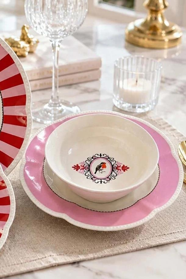 Kuş motifli pembe-beyaz kase, pembe tabak ve şarap kadehinden oluşan masa düzenlemesi.